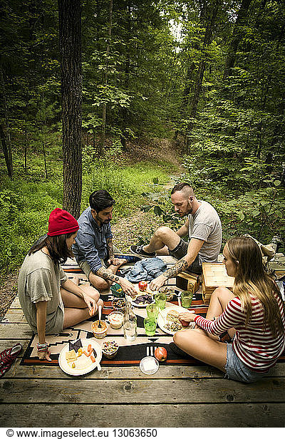 Hochwinkelansicht von Freunden  die Essen essen  während sie auf einer Veranda im Wald sitzen