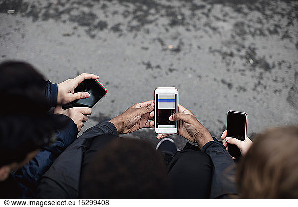 Hochwinkelansicht von männlichen Freunden  die soziale Medien nutzen  während sie auf der Straße sitzen