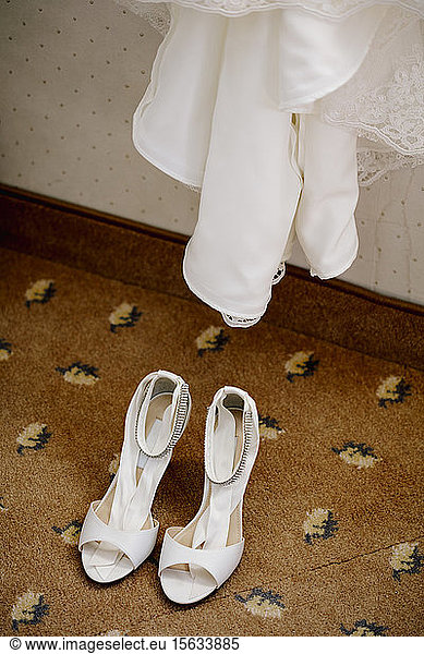 Hochwinkelansicht von Sandalen auf Fliesenboden unter dem Brautkleid zu Hause