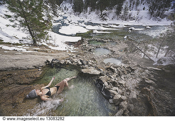Hochwinkelaufnahme einer Frau im Bikini  die sich im Winter im Thermalbad im Wald entspannt