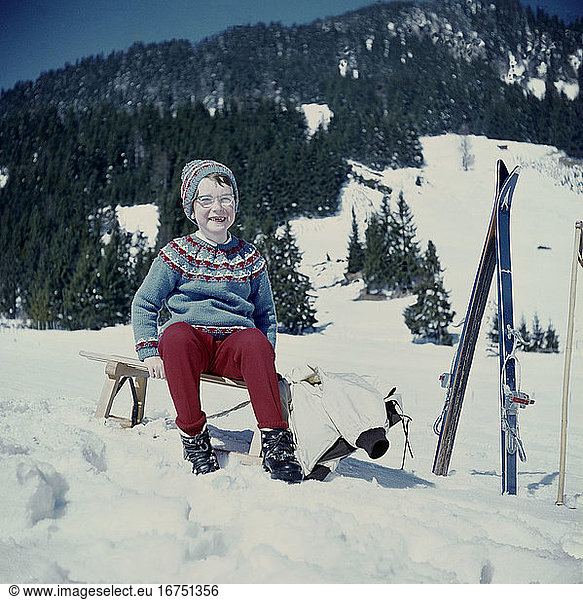 Holidays and leisure time:
winter holiday. A young girl with a sledge and skis; in the background a mountain range. Amateur photo  Germany  undated
(c. 1960s).