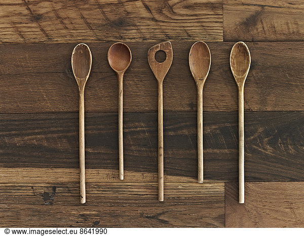 Home cooking. A wooden table with a varied wood grain and colour. Five wooden spoons in a row.