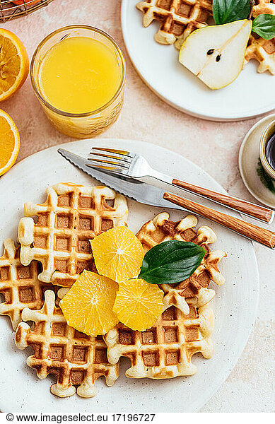 homemade waffles on a light pink background. orange juice. fruit