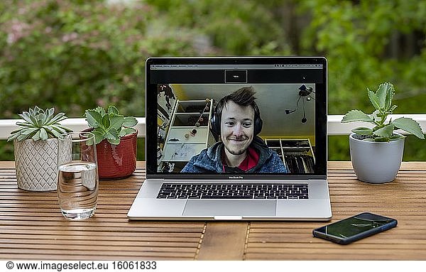 Homeoffice mit Laptop  Apple MacBook Pro und iPhone X am Schreibtisch  mit Programm Zoom während einer Videokonferenz  Deutschland  Europa