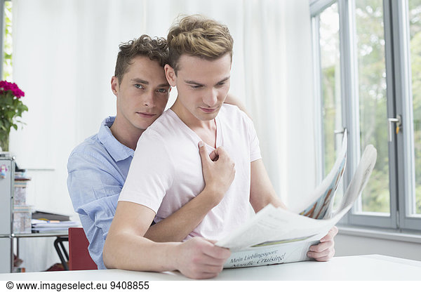 Homosexual couple embracing each other while reading newspaper