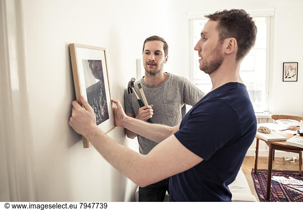Homosexual couple hanging picture frame on wall at home