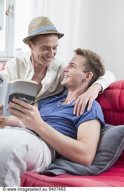 Homosexual couple sitting on couch with book  smiling