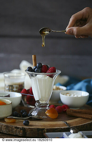 honey dripping from spoon onto fruit and yogurt parfait