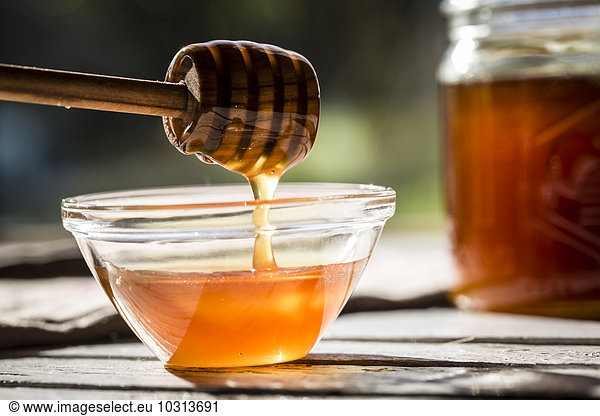 Honig  der von einem Honiglöffel in eine Glasschale tropft.