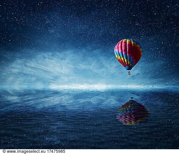 Hot air balloon flying over the a cold dark blue sea. Wonderful landscape with a starry night sky background and water reflection