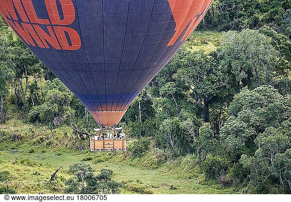Hot air balloon with tourists in low flight over savanna and forest. Masai Mara National Reserve  Kenya  Africa