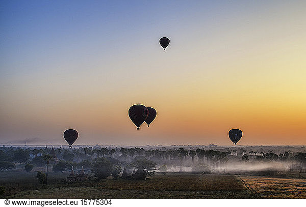 Hot air balloons over landscape with distant temples at sunset  Bagan  Myanmar.