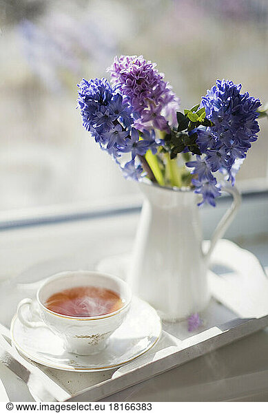 Hot tea in vintage cup by flower vase at home