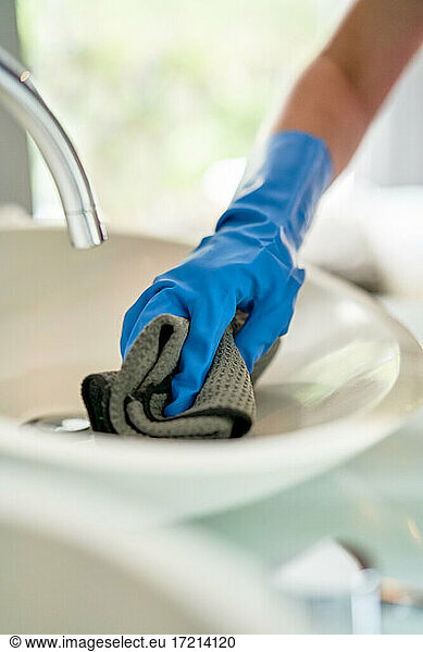 Hotel maid in gloves cleaning hotel room bathroom sink