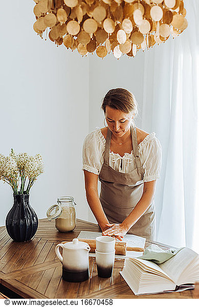 Housewife preparing dough standing at domestic kitchen  wearing apron
