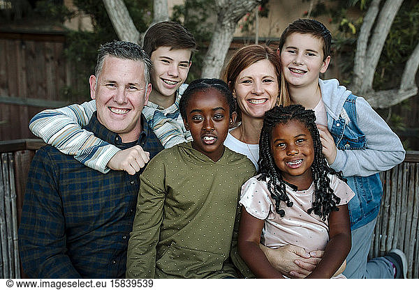 Hugging happy multiracial family smiling in front of tree