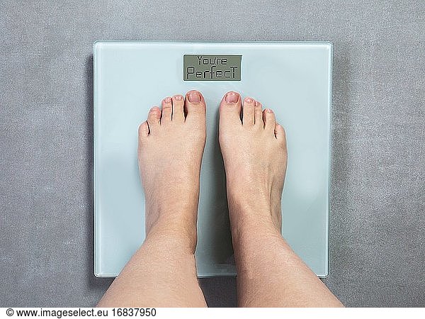 Human Feet auf digitaler Waage mit den Worten You're Perfect  Selbstvertrauen und Diät-Konzept Draufsicht pn grauen Boden Hintergrund.