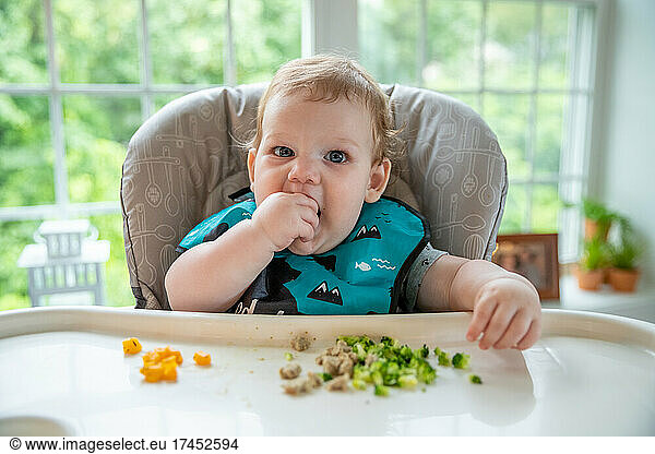 Hungry baby boy putting food in his mouth with his hands.
