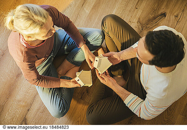 Husband and wife holding house models sitting cross-legged at home