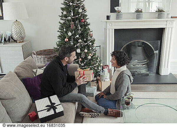 Husband giving Christmas gift to wife by tree in living room