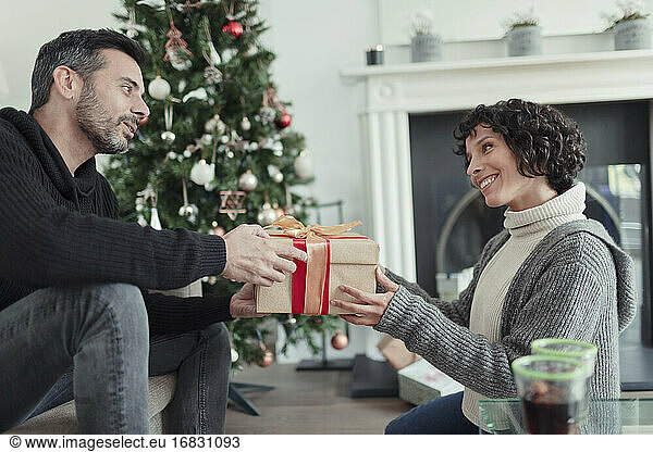 Husband giving Christmas gift to wife in living room with tree