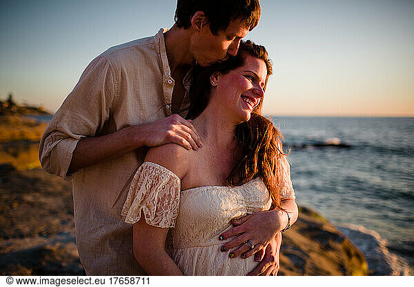 Husband Kissing Pregnant Wife on Beach at Sunset in San Diego