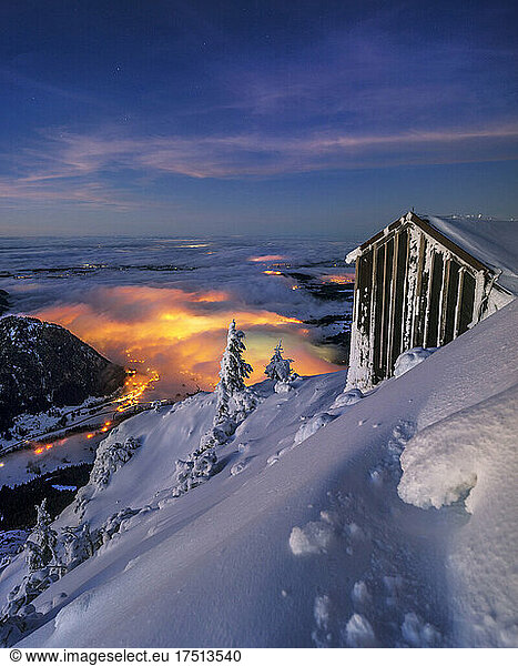 Hut in snowcapped mountains at night with lights in distance