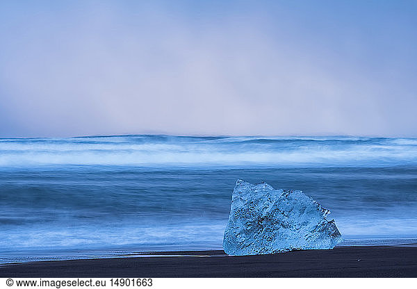 Ice chunk on the shore of the ocean with waves crashing against the shoreline; Iceland