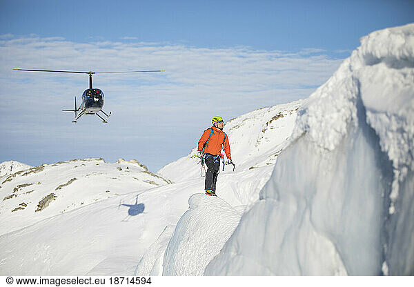 Ice climber looks at his next challenge  helicopter behind.