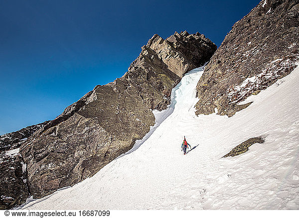 Ice climber walking towards ice gully with skis on back