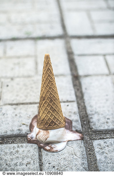 Ice cream cone with melting scoop upside down on the ground