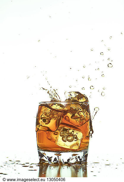 Ice cubes splashing in whiskey over white background