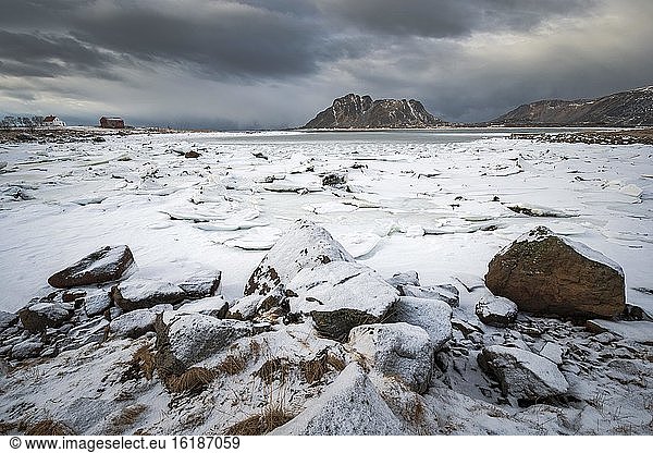 Ice floes behind rocks at the frozen fjord in a dark cloud atmosphere  mountains  Vesteralen  Nordland  Norway  Europe