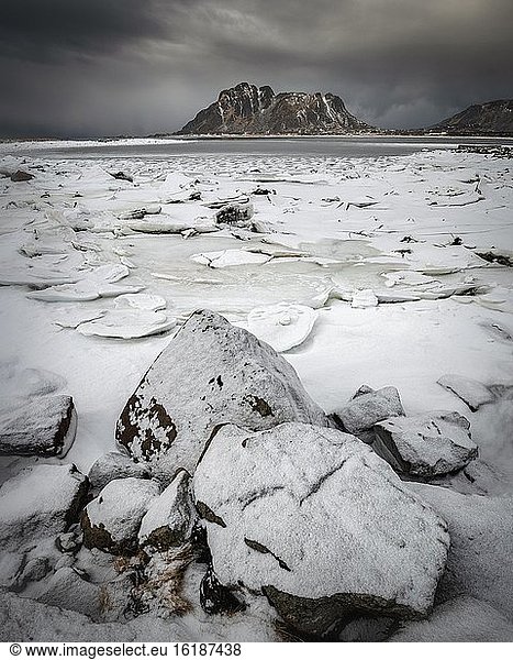 Ice floes behind rocks at the frozen fjord in a dark cloud atmosphere  mountains  Vesteralen  Nordland  Norway  Europe