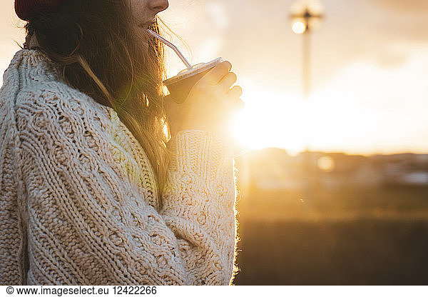 Iceland, young woman with coffee to go at sunset