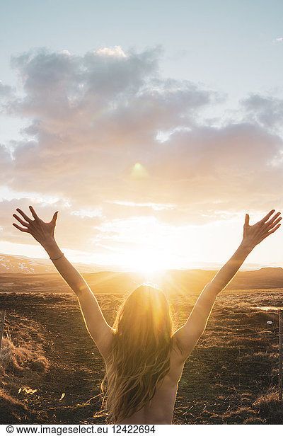 Iceland, young woman with raised arms at sunset, Iceland, young woman with raised arms at sunset