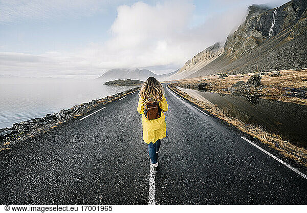 Iceland  back view of woman with backpack walking on median strip of country road