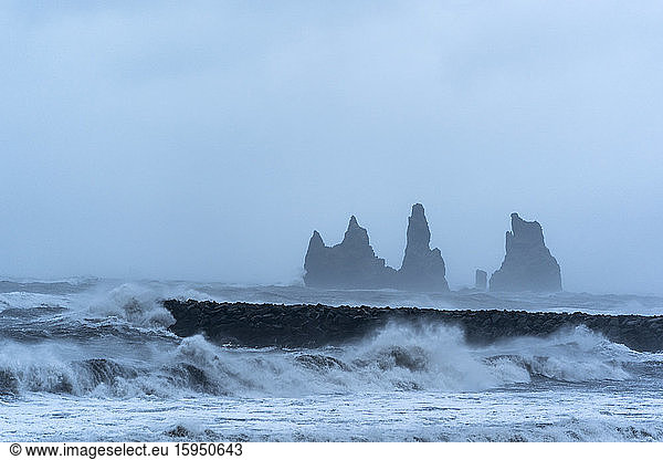 Iceland  Hofn  Sea waves splashing against coastal stone wall with stack rocks in background