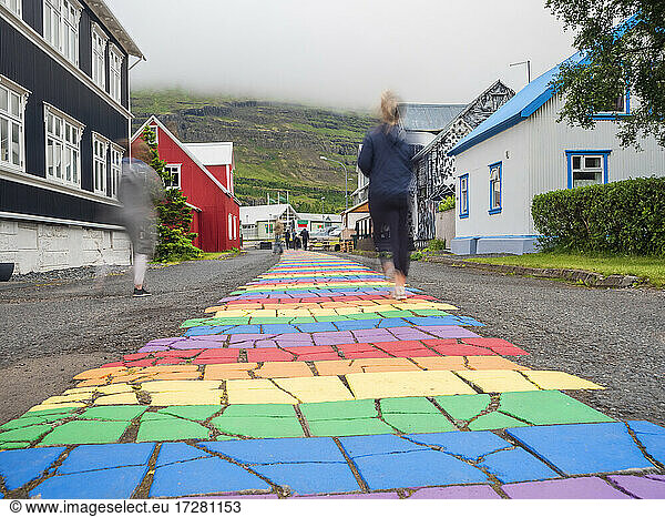 Iceland  Seydisfjordur  People walking along rainbow colored asphalt road in middle of secluded town