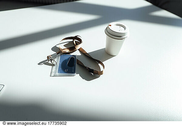 ID Card and disposable cup on white desk in sunlight