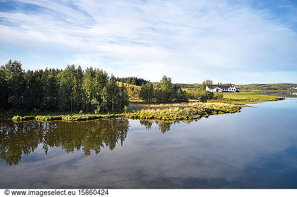 Idyllische Flusslandschaft mit Laubwald und einsamem Landhaus an sonnigen Sommertagen