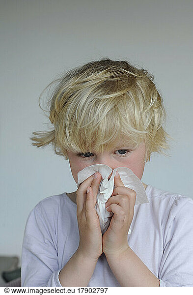 Ill girl with facial tissue cleaning nose at home