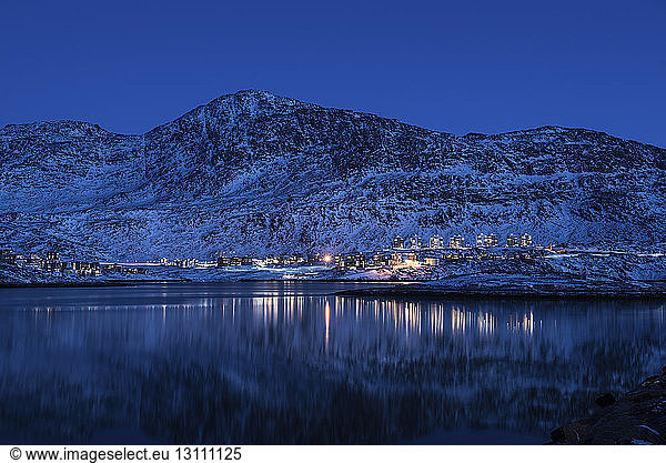Illuminated buildings by sea against snowcapped mountain at night