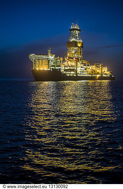 Illuminated drill ship on sea against blue sky at night