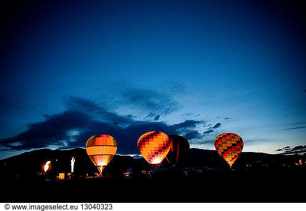 Illuminated hot air balloons on field against blue sky at dusk