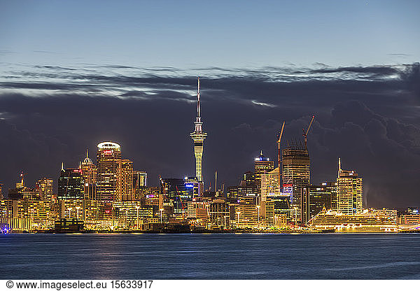 Illuminated modern buildings by sea against cloudy sky at dusk in Oceania  New Zealand
