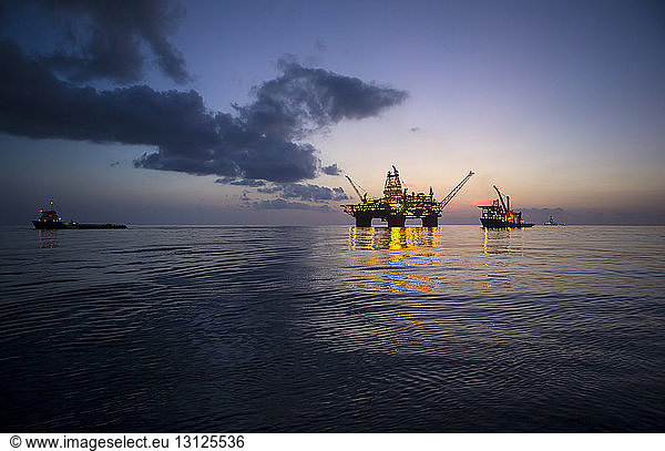 Illuminated offshore platform against sky at dusk