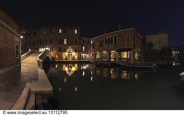 Illuminated residential buildings by canal in city at night