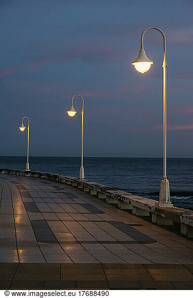 Illuminated street lights on promenade by sea
