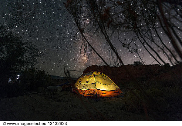 Illuminated tent on field against star field at night